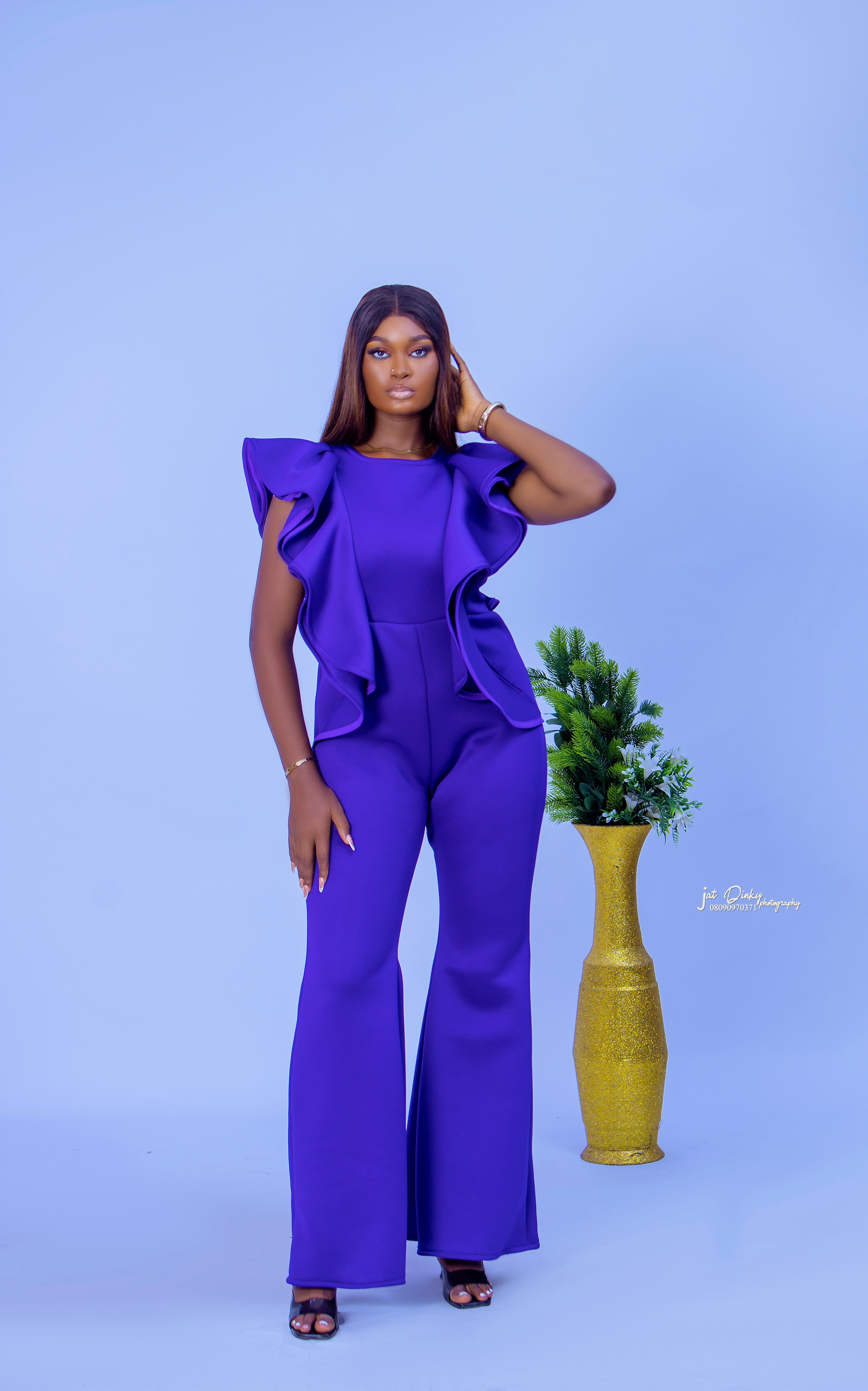 A woman standing and posing in a vibrant purple jumpsuit with bold ruffle sleeves ready to wear & classic.